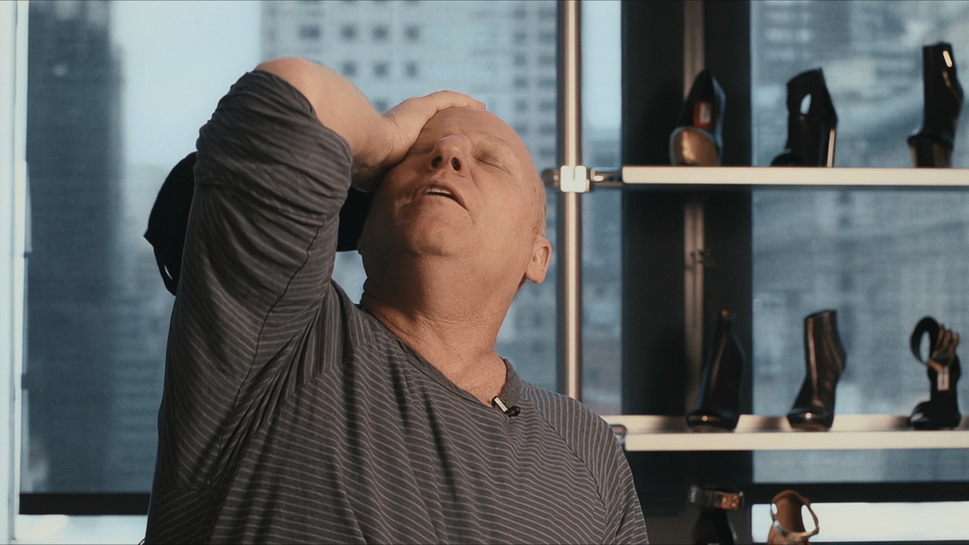 A man with a hand on his head, laughing, beside a shelf of heels, Maddman