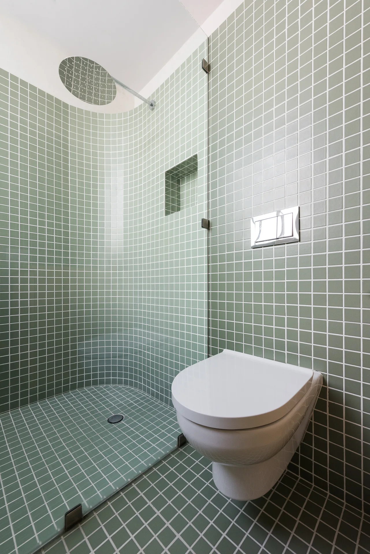 Inodoro y muro de mosaico verde junto a la ventana del baño