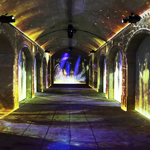 一个灯光昏暗的拱形走廊,墙壁和天花板上投影着人影和图案,呈现出色彩斑斓的灯光展示。