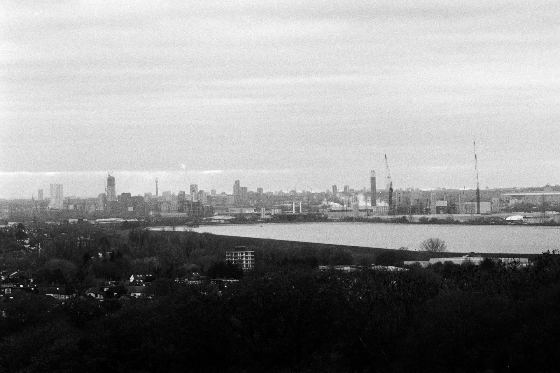 London skyline with reservoirs and industrial cranes viewed from elevated position across suburbs