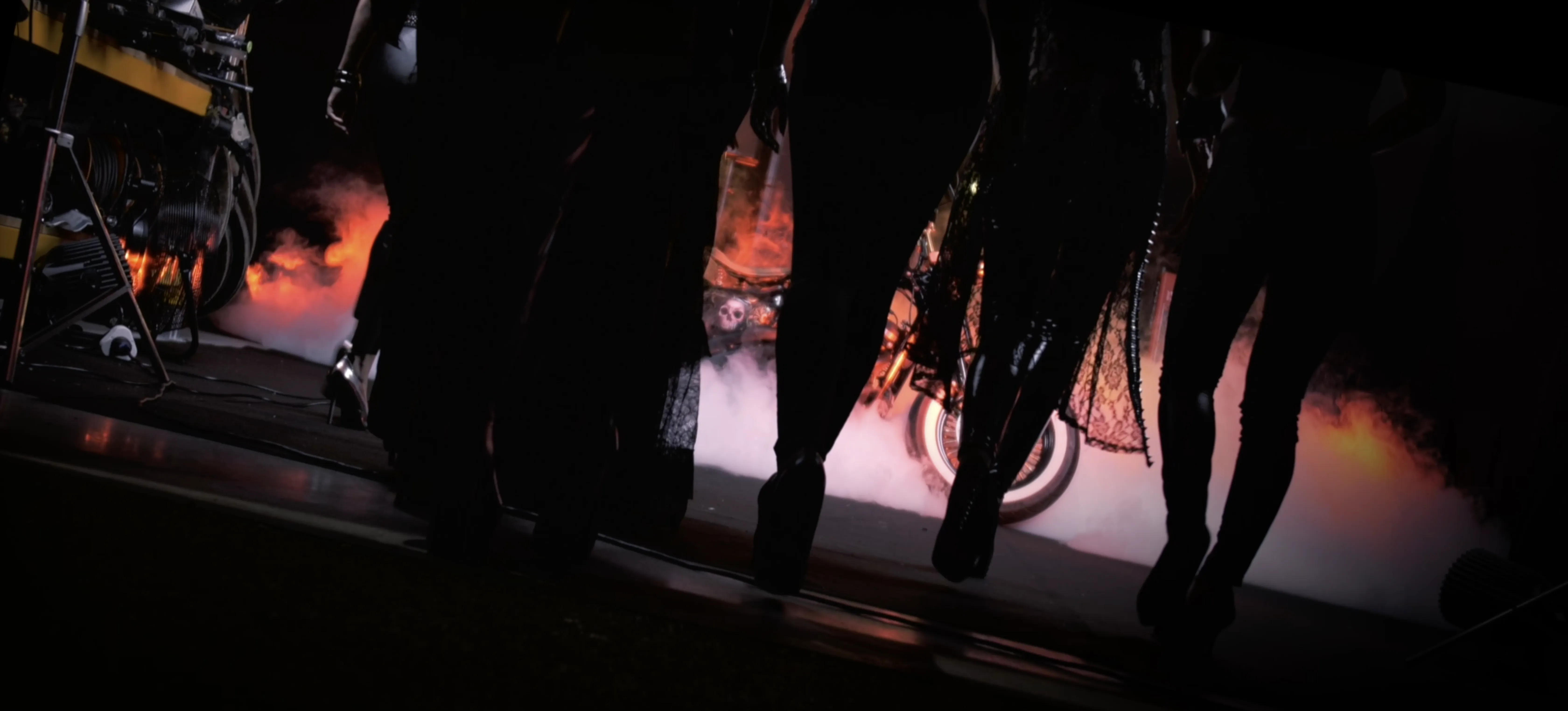 A group of people walk towards a motorbike enveloped in dramatic orange smoke, creating a mysterious and intense atmosphere.
