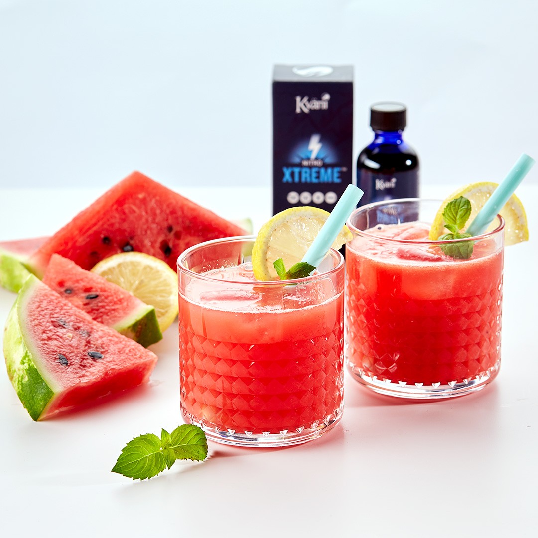 Two glasses of vibrant watermelon juice garnished with lemon slices and mint leaves, accompanied by fresh watermelon slices and Kyäni Xtreme products in the background, creating a refreshing and invigorating display.