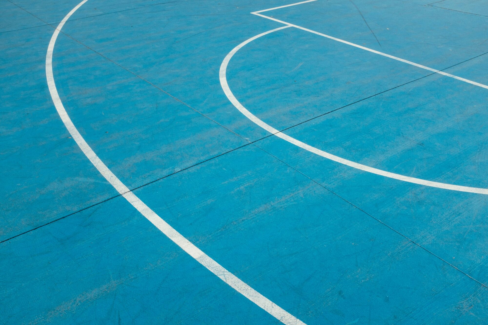 Curved white lines on a vibrant blue surface, resembling a sports track or court layout.