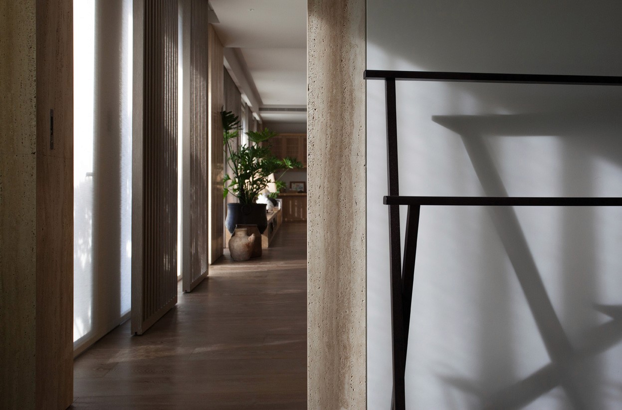 木質走廊一側擺放陶盆與植栽，自然光穿透百葉窗投射於地板與牆面上