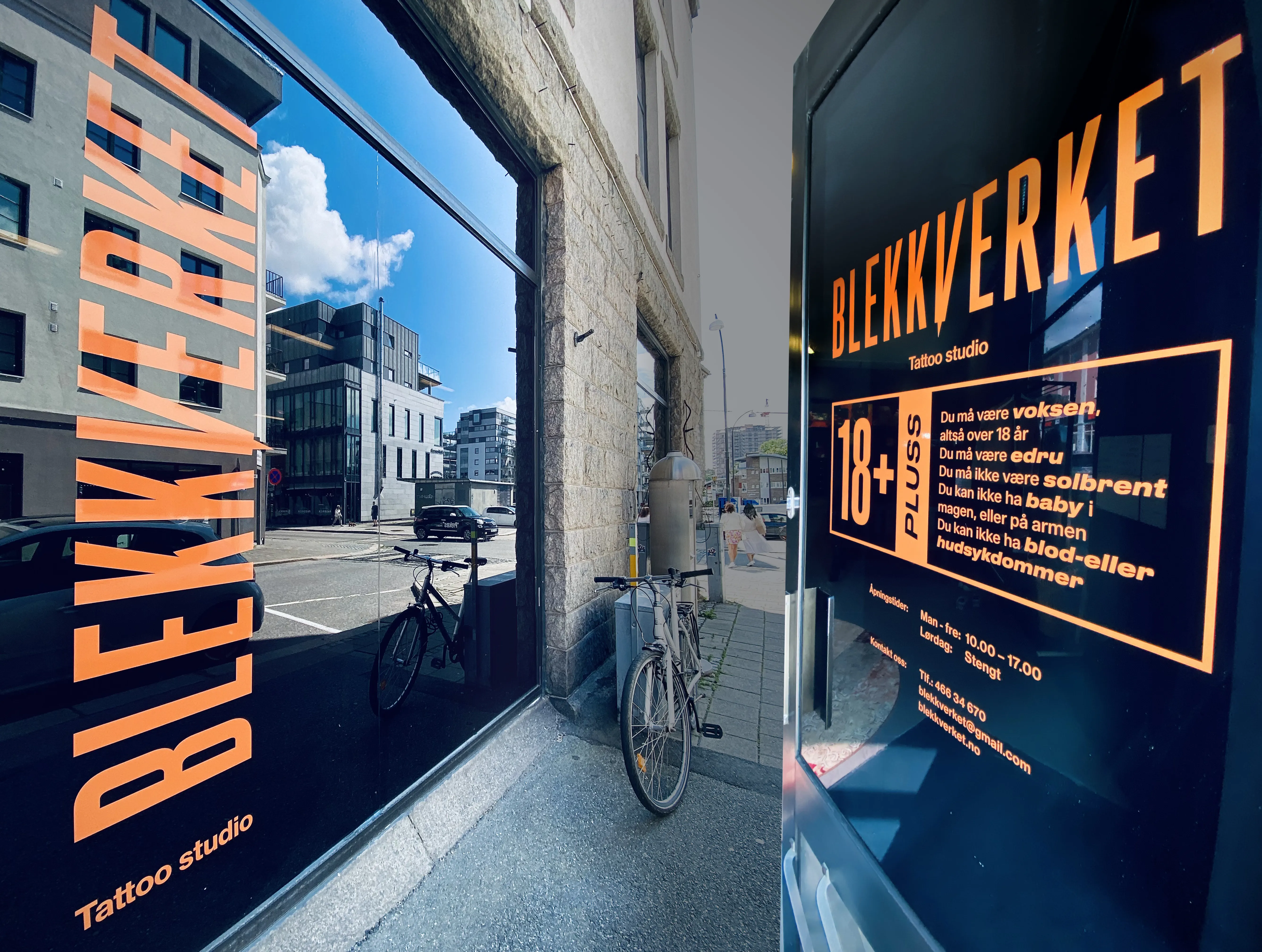 Oransje vindusdekor og dørdekor for Blekkverket Tattoo studio på svart bakgrunn mot gaten
