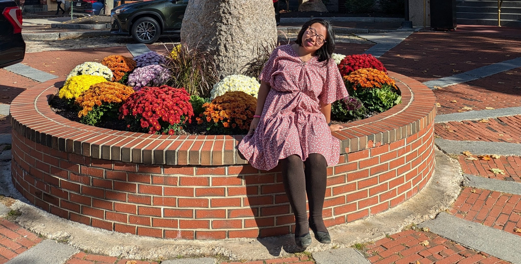 Lizy sitting on a brick ledge with a pink dress covered in hearts