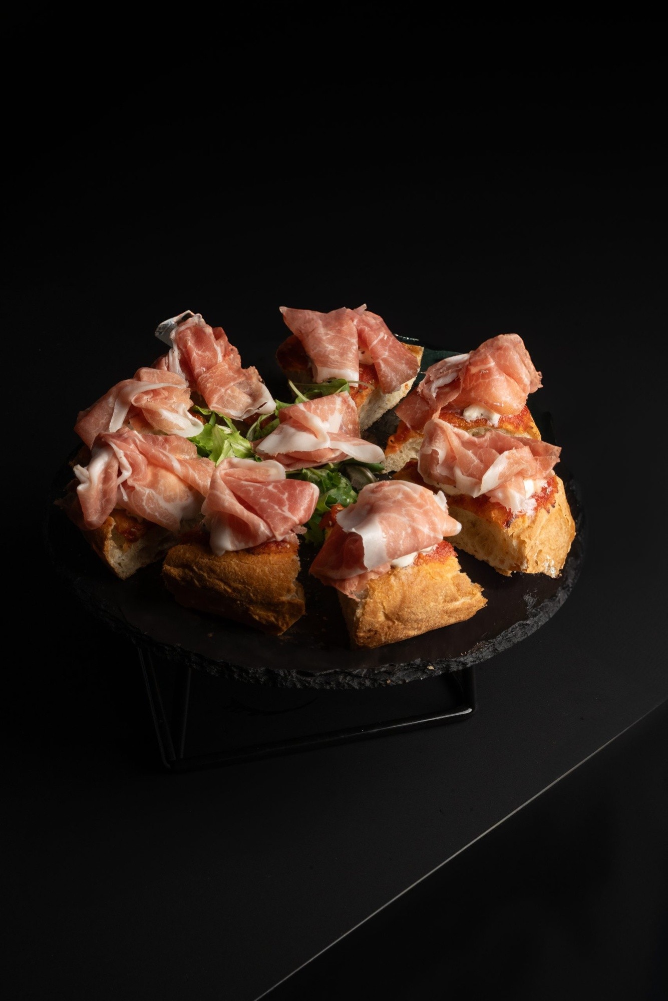 Pizza tagliata a pezzi con crudo di Parma 24 mesi e stracciatella su vassoio in ardesia scura