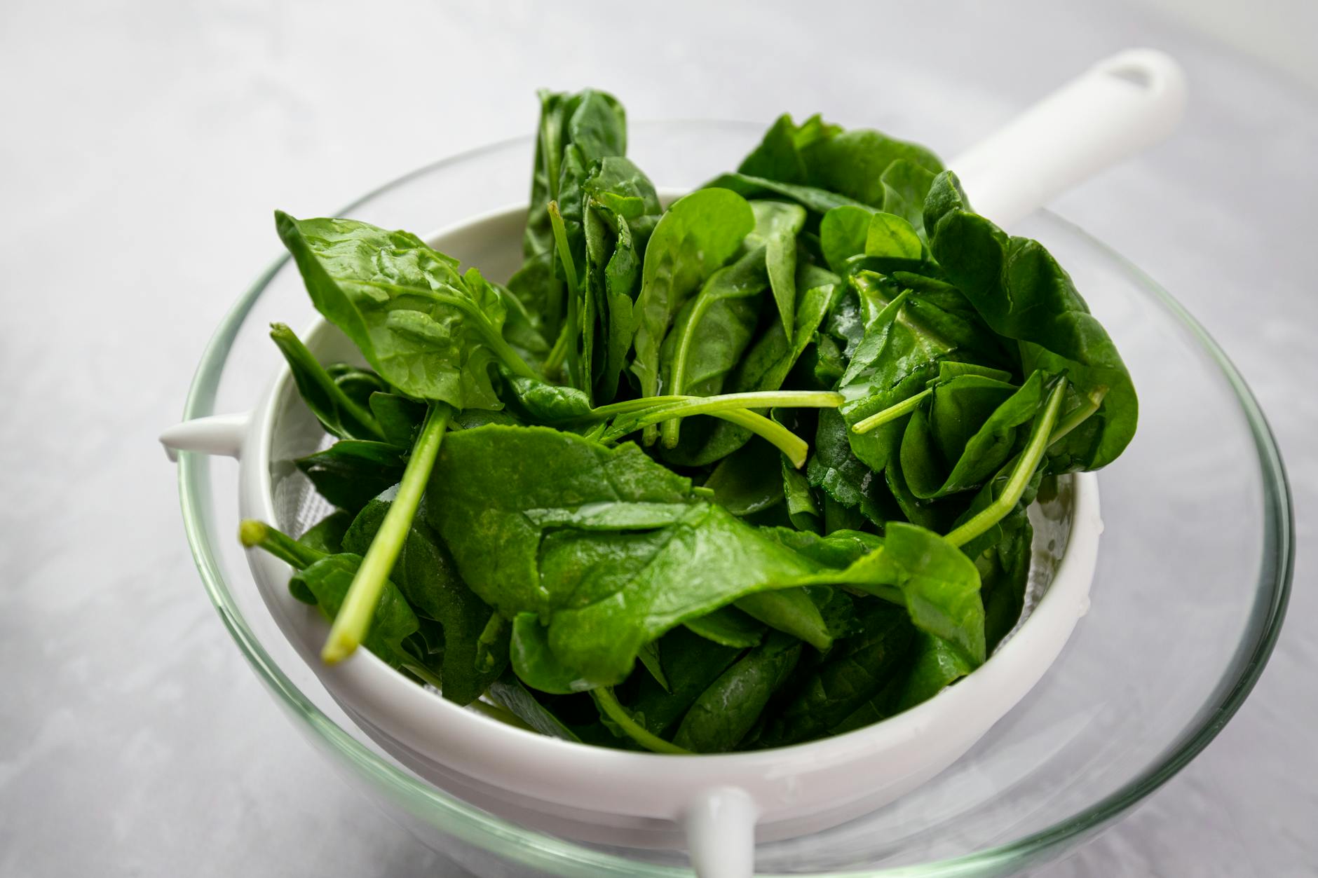 Fresh spinach leaves in a white strainer for healthy homocysteine-lowering meals