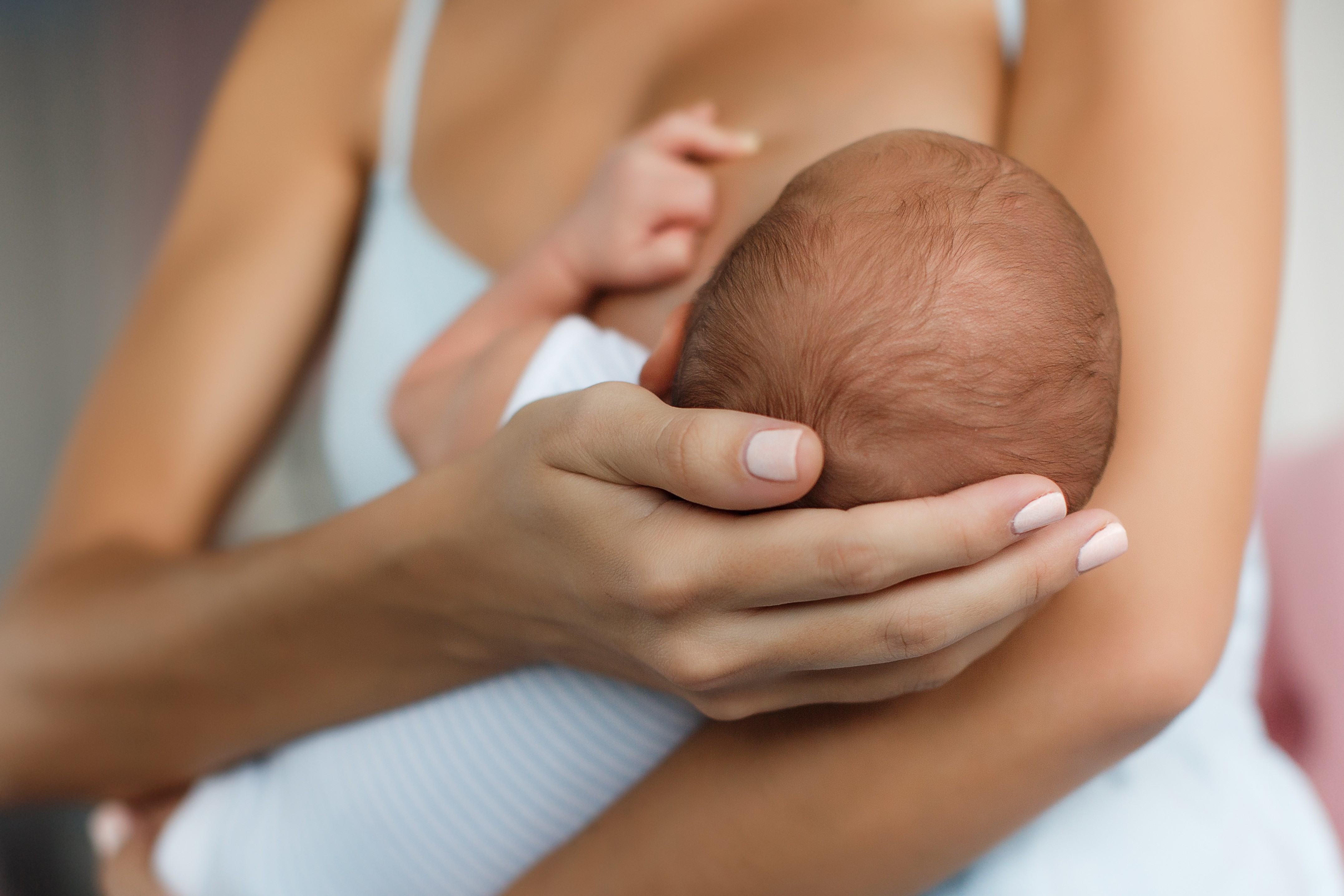 Mother in a white top cradling her newborn baby's head in her hands