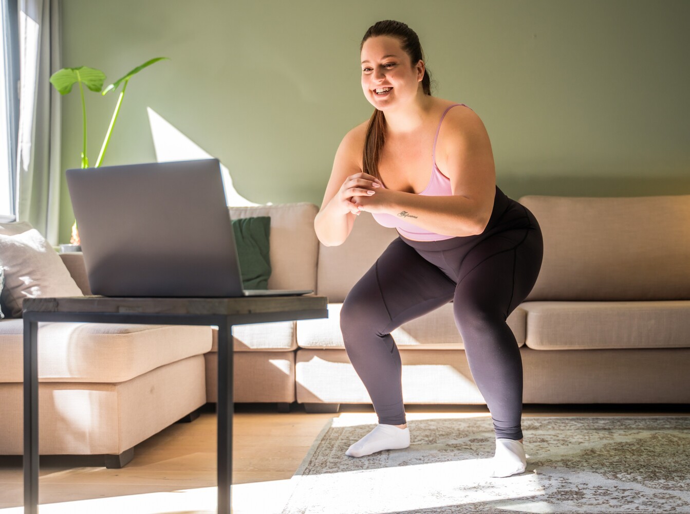 woman doing squats during a beginner-friendly home workout for weight loss while she follows instructions on her laptop