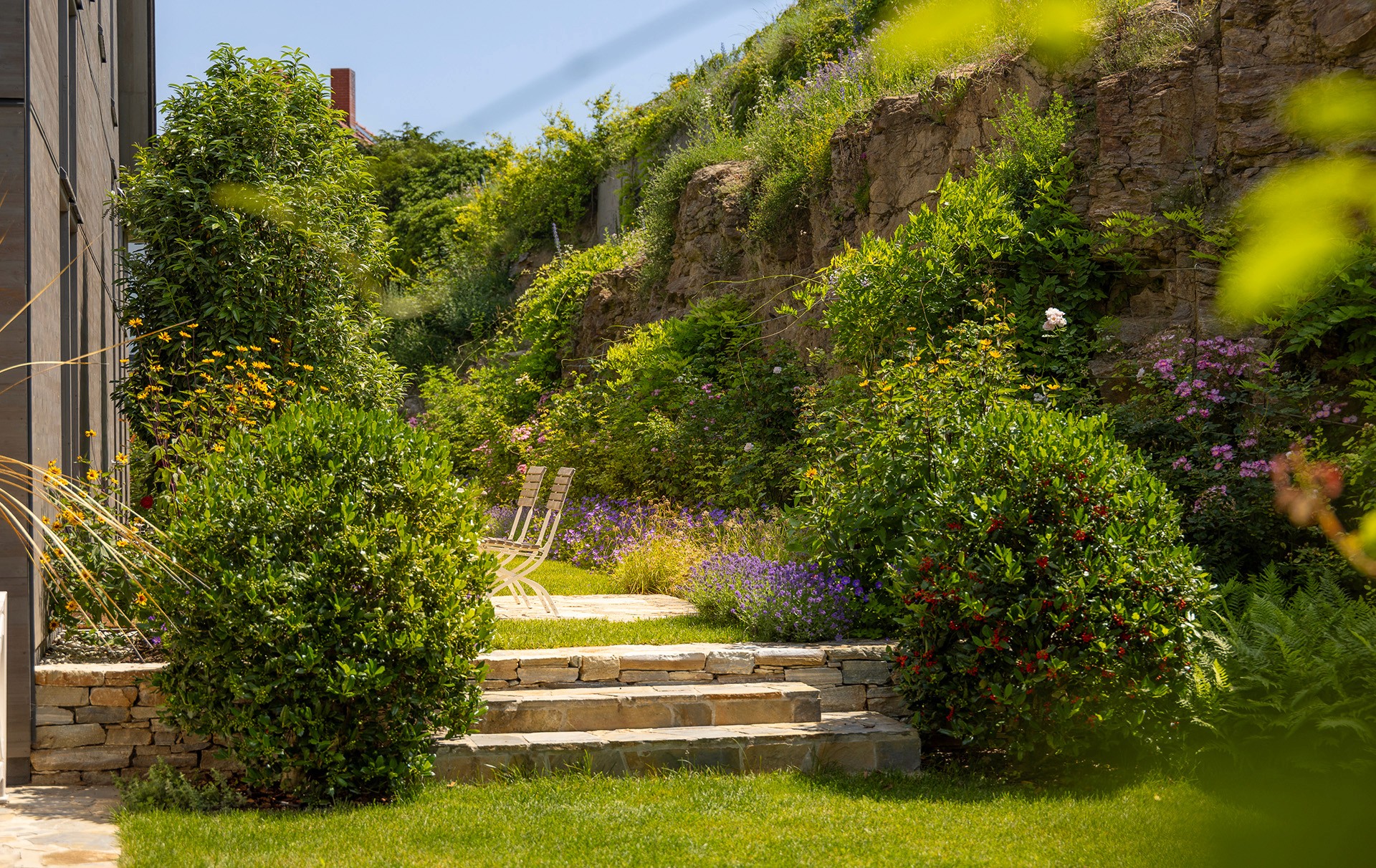 Gartenbereich mit Naturstein-Stufen, dicht bepflanztem Hang und ruhigem Sitzplatz.