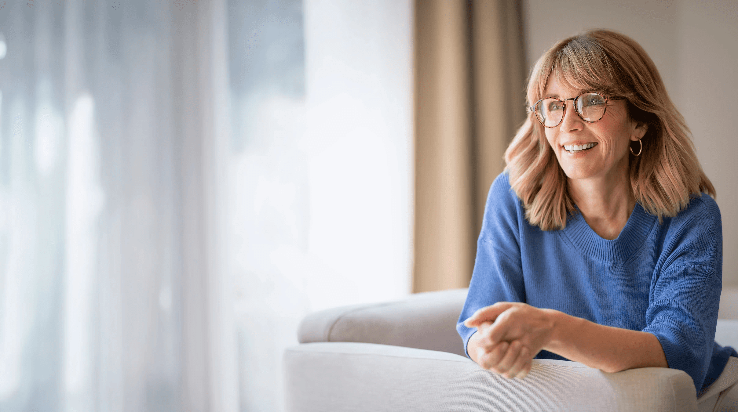 Woman 40+ smiling, sitting next to the window, representing Flouria’s Postmenopause care