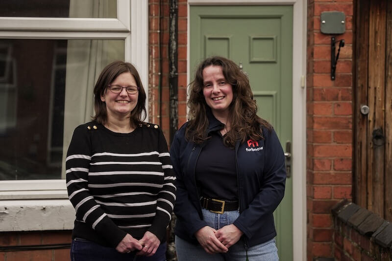 Two people smiling outside the front door to a home.