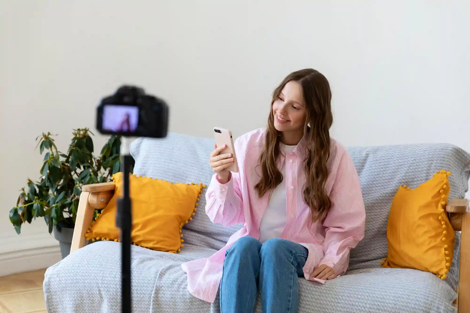 Lifestyle creator sits on a couch, holding a phone while recording a video for her online audience.