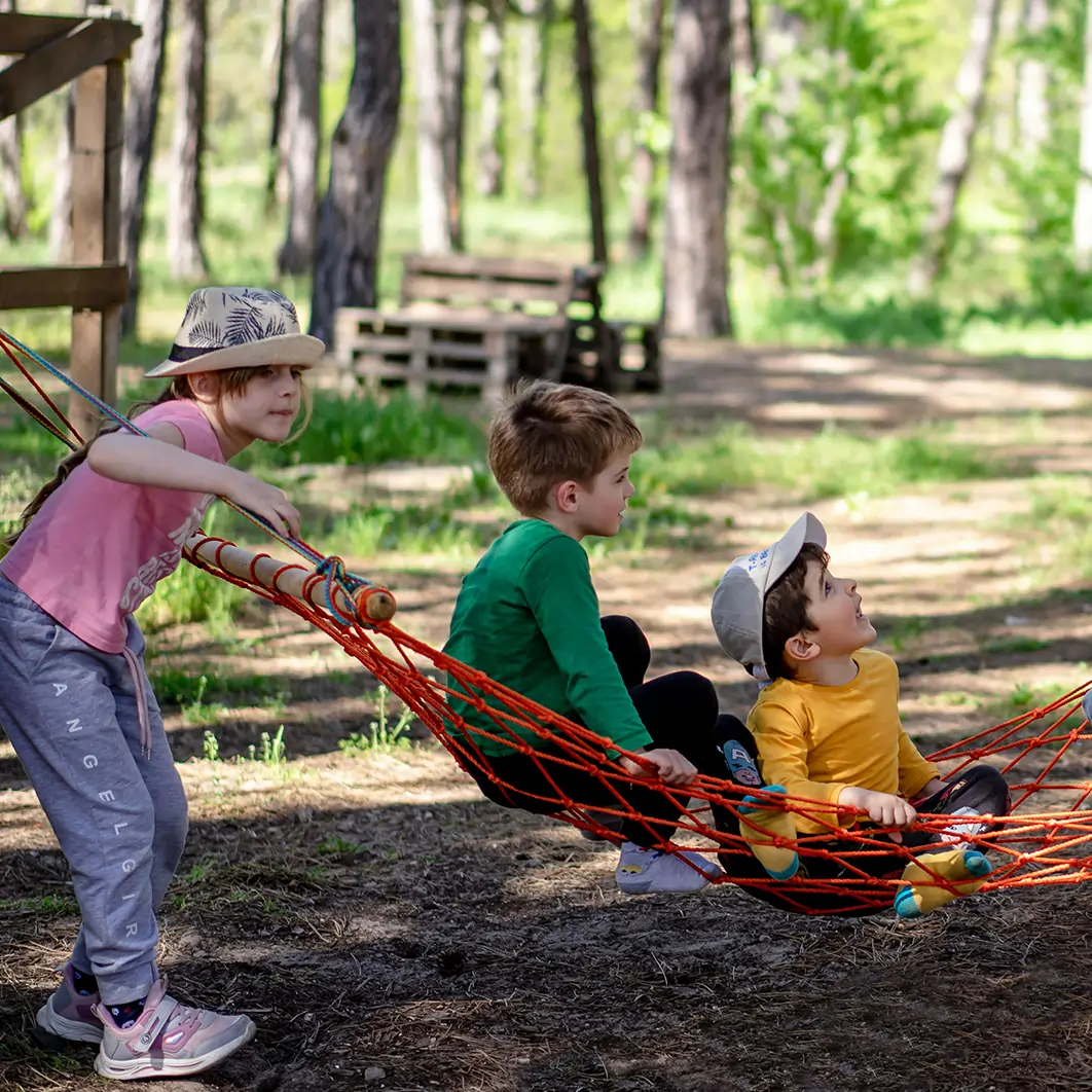 Group of children outdoors, swinging in a hammock. 