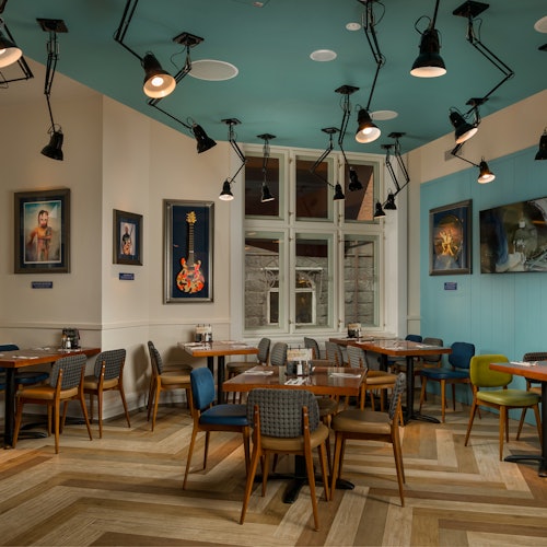 En stilfuld, tom café med moderne indretning indeholder træborde, stole i forskellige farver, vægkunst og talrige loftslamper.