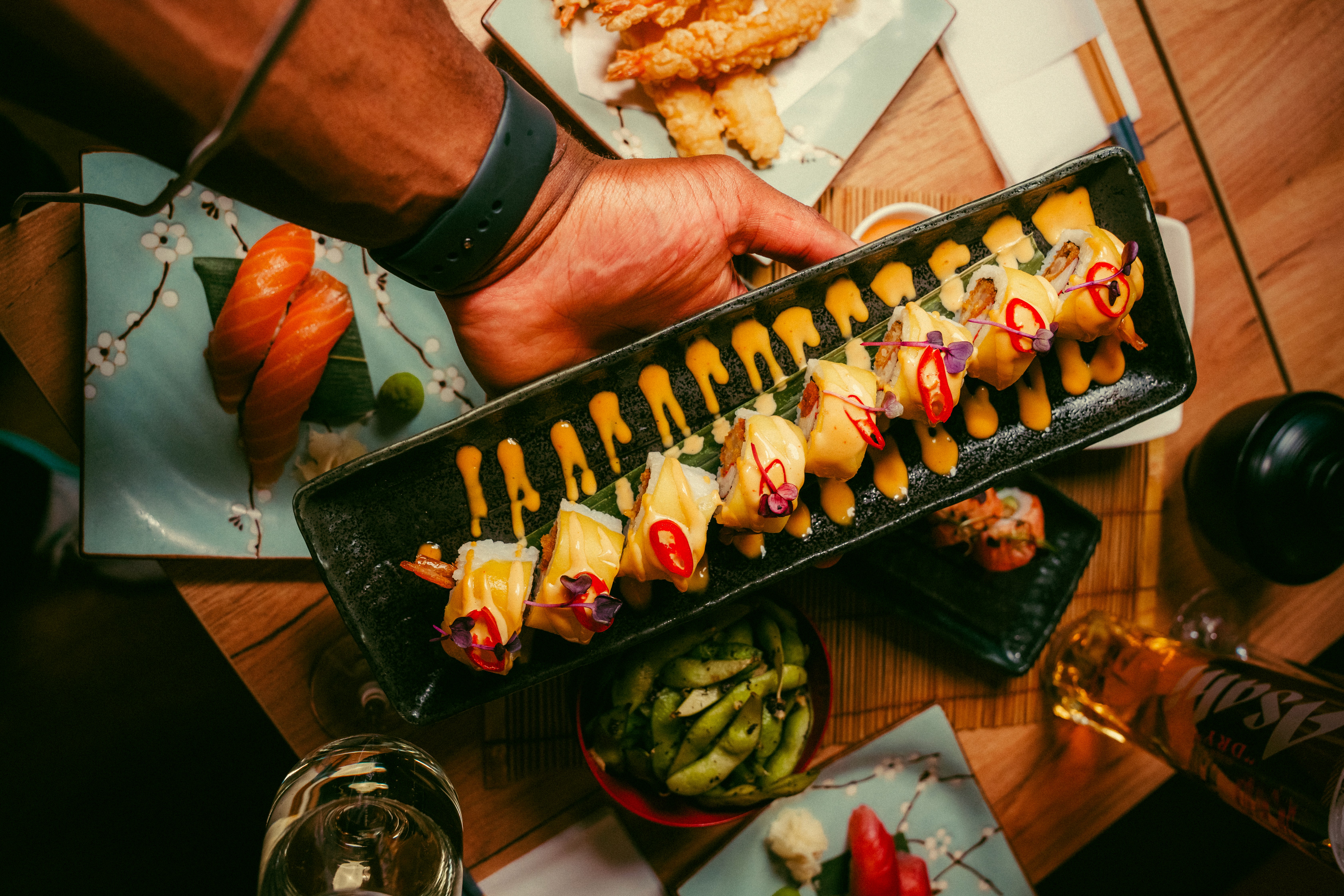 remium bottomless sushi and cocktails at East London's No.1 Japanese restaurant. A wooden platter of signature sushi rolls and a green matcha cocktail, part of a £49 unlimited dining experience in London