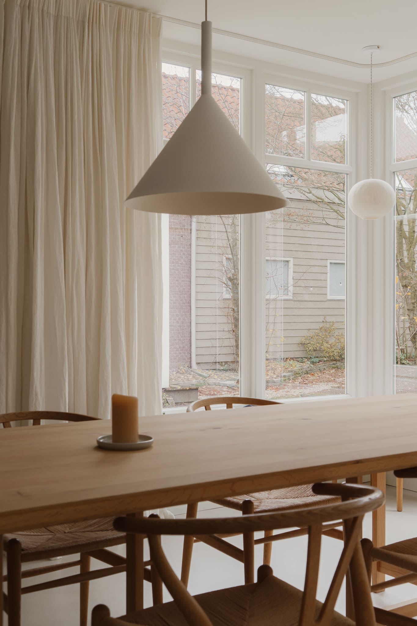 Lichte eetkamer met een grote eikenhouten eettafel, design stoelen en kamerhoge linnen gordijnen, ontworpen door interieurontwerper in Delft.