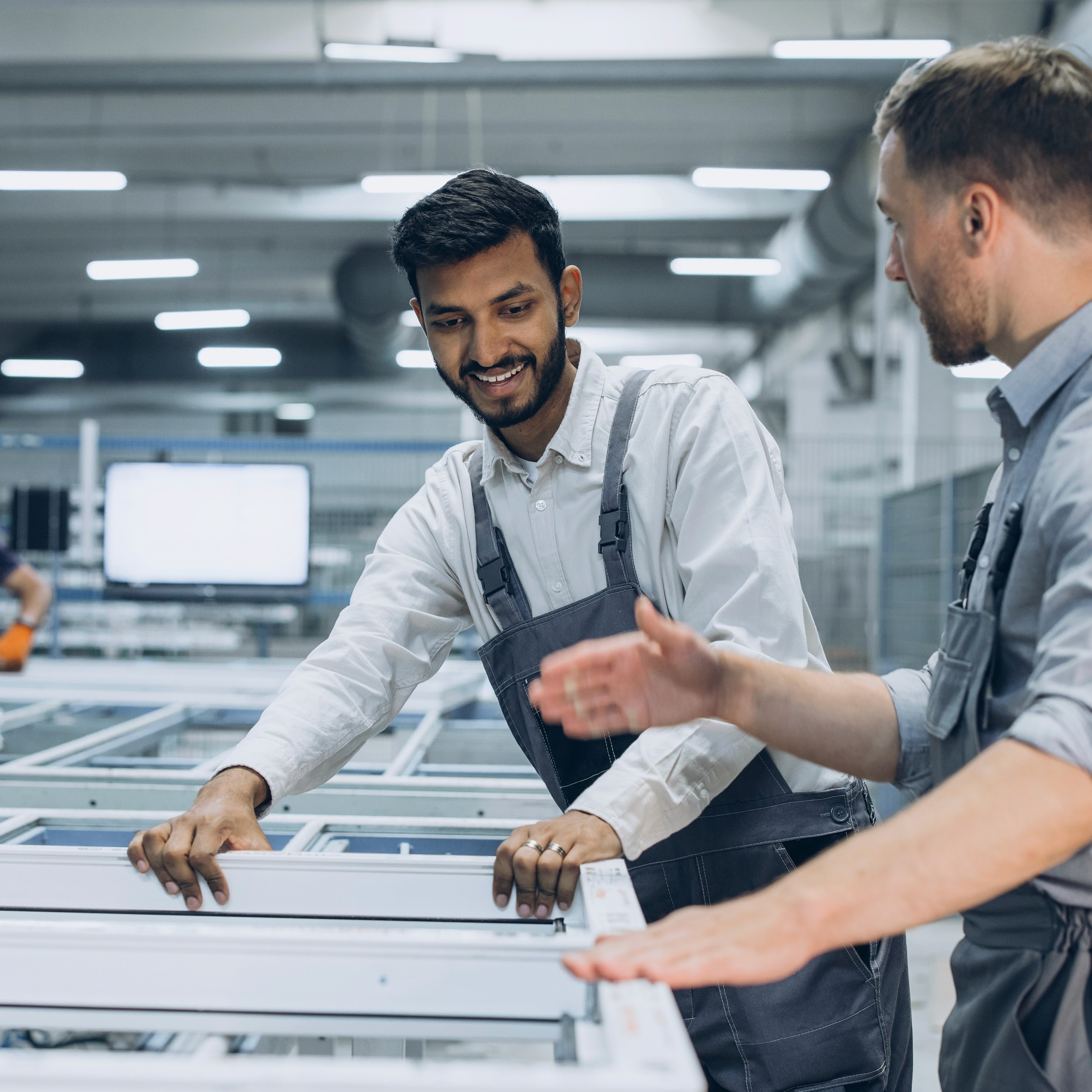 Drei Arbeiter besprechen Maschinen in einer hellen Industrieumgebung und demonstrieren dabei Teamwork und Zusammenarbeit.