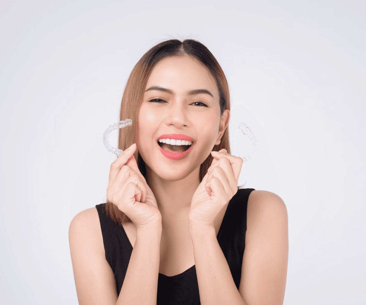 Invisalign in Dubai with a woman smiling confidently, holding her clear aligners, highlighting discreet and effective treatment.