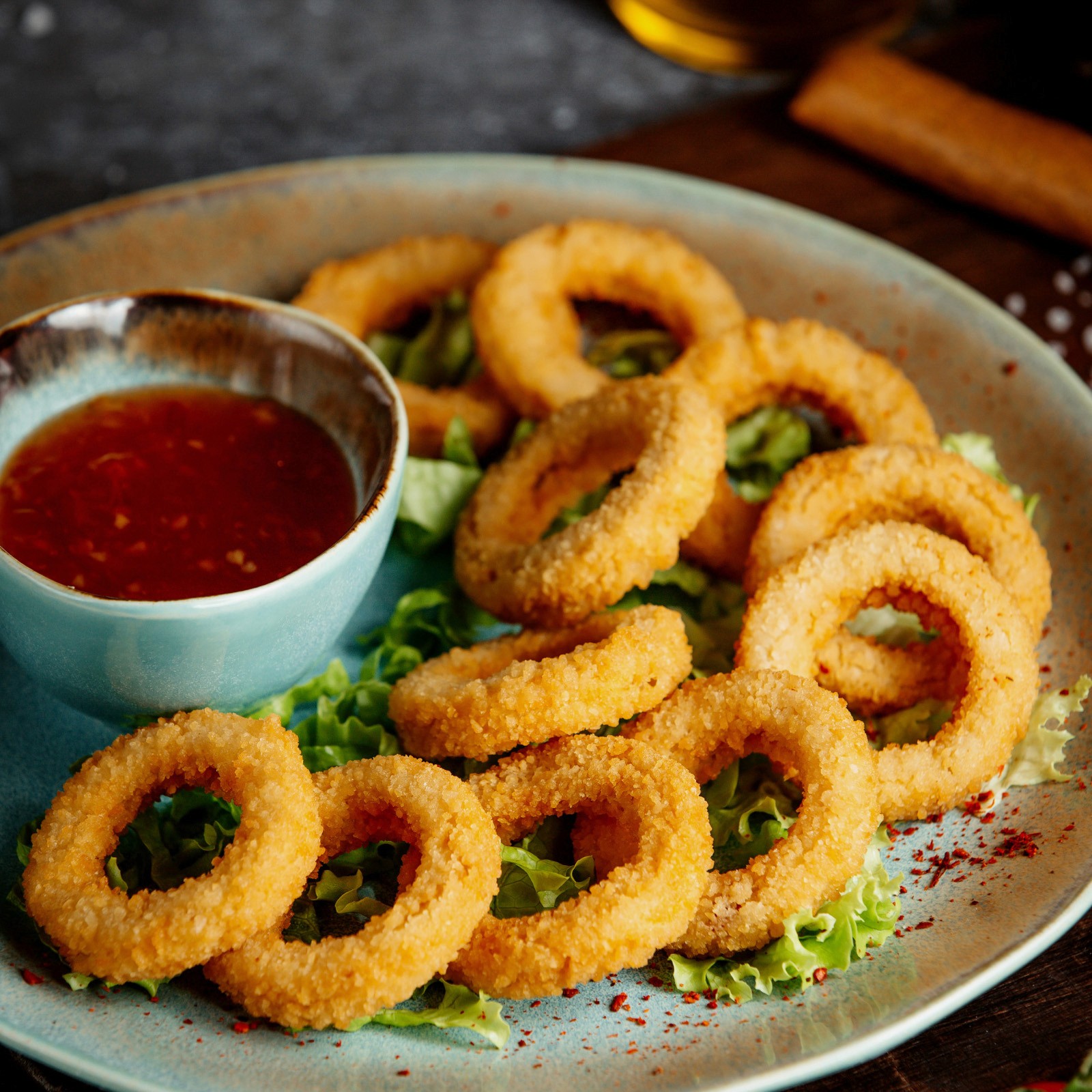 Fried onion rings on a bed of lettuce, served on a light blue plate with a side of red dipping sauce.