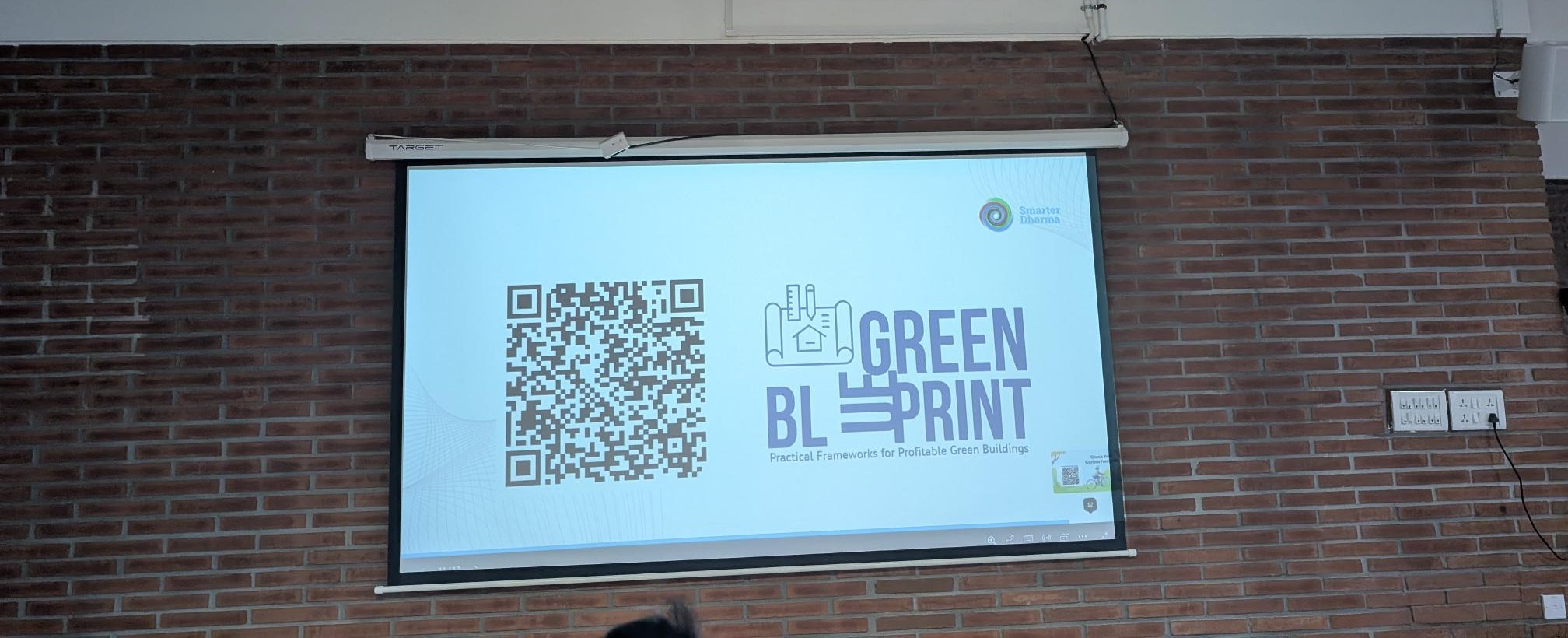 A man stands while two people sit at a table in an office setting, smiling and engaged in conversation. The mood is friendly and collaborative.