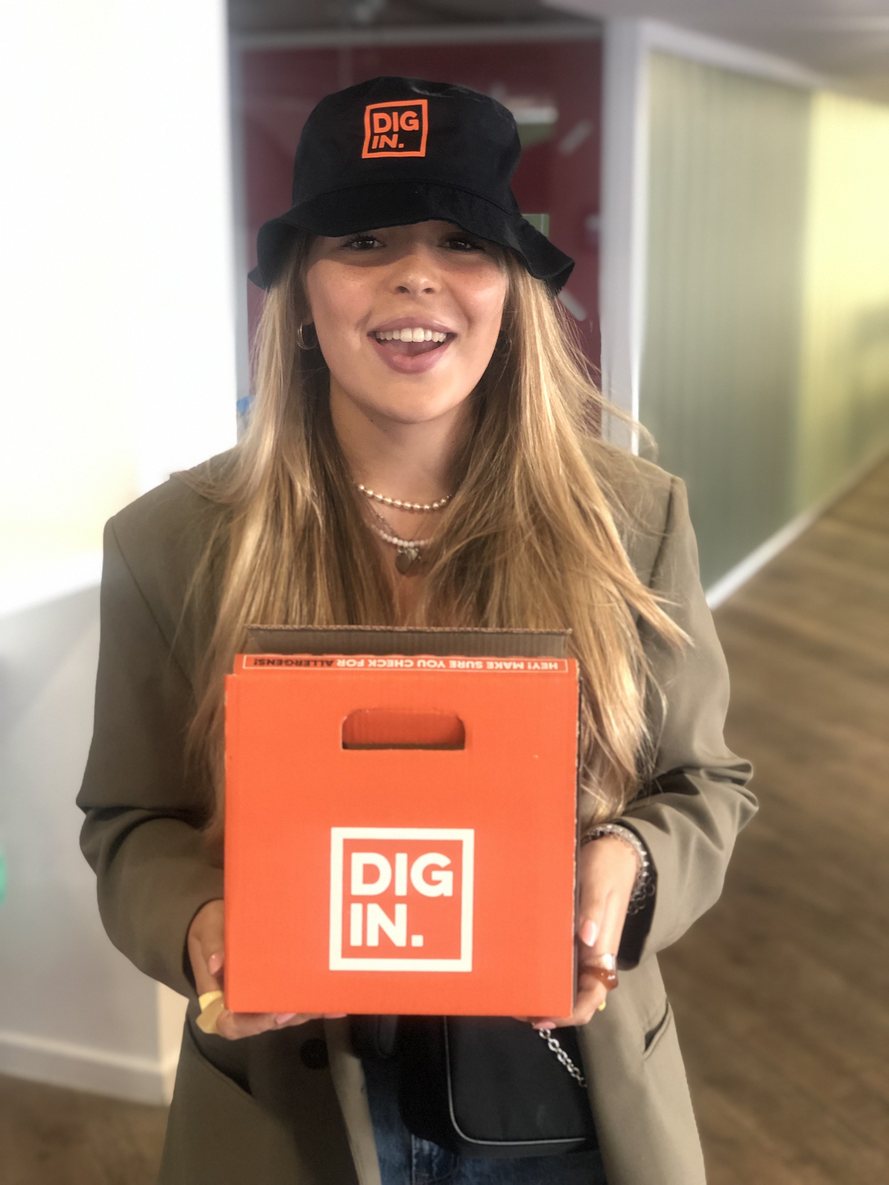 Student in a Dig In bucket hat holding a Dig In box
