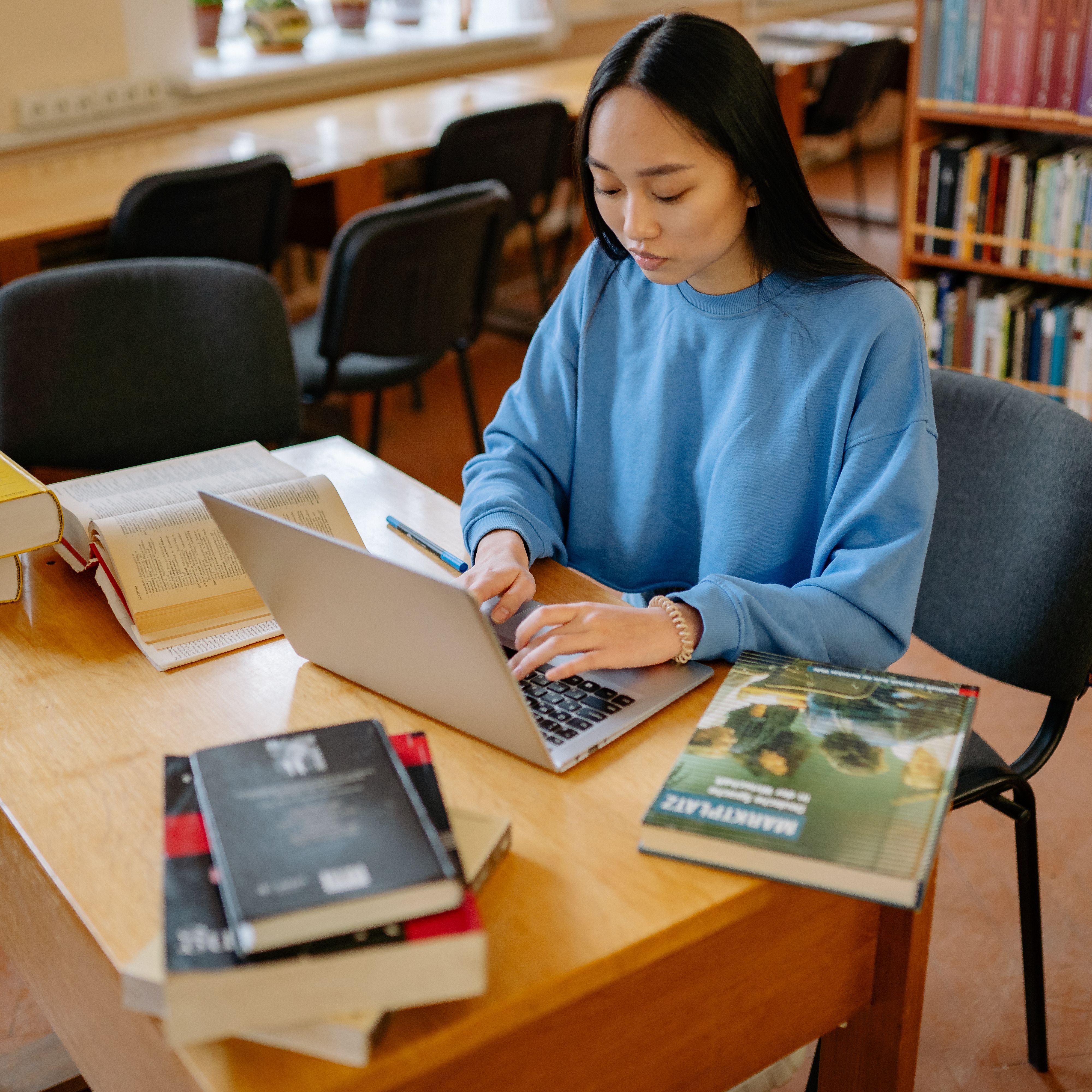 asian-woman-typing-on-a-laptop-surrounded-by-books-in-a-library-setting. - yan-krukau (pexels)