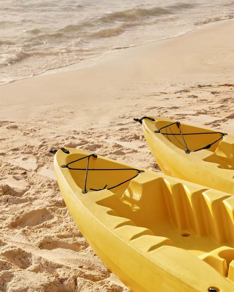 Two yellow kayaks lying on a sandy beach near the water.