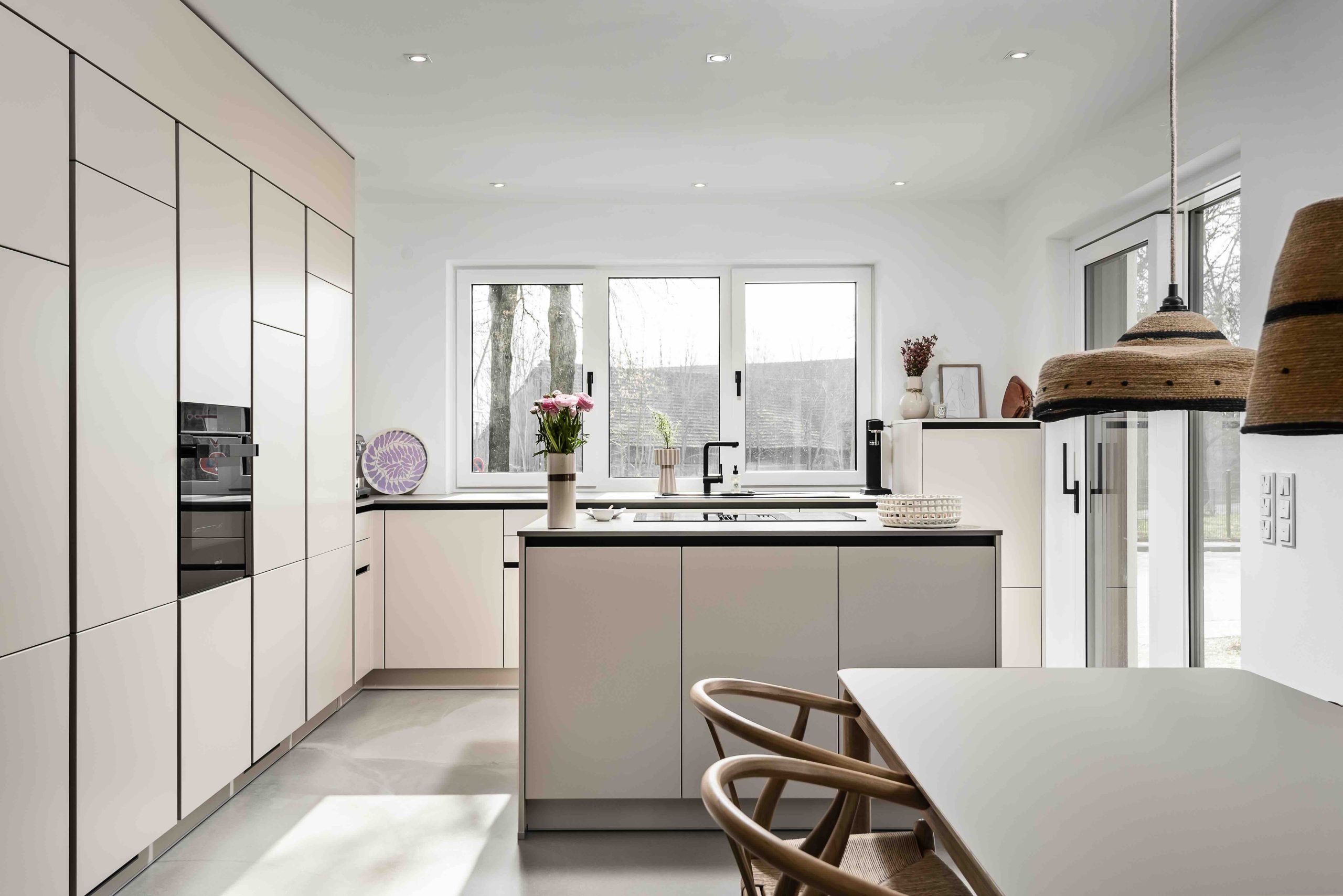 Helle, moderne Küchen mit cremefarbenen Fronten und einer Kücheninsel, die durch natürliche Lichtakzente betont wird.