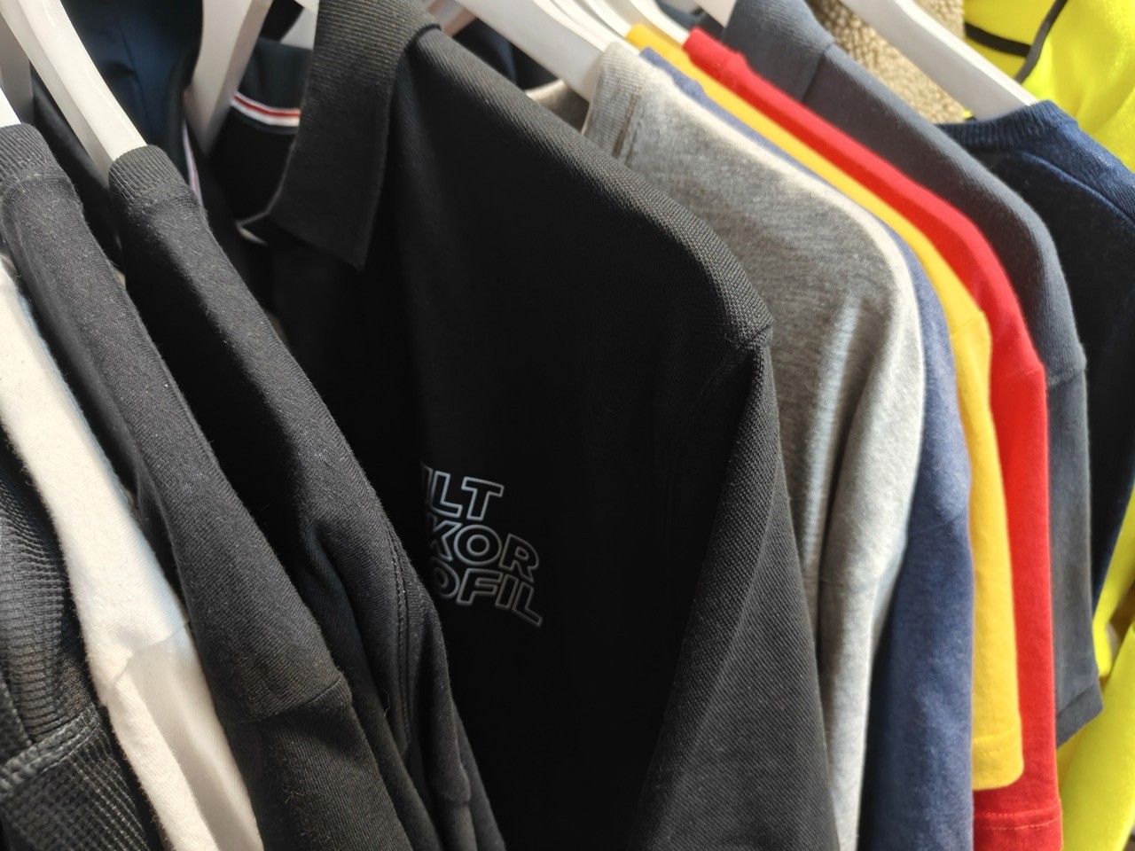 En rekke uformelle poloskjorter i ulike farger, inkludert svart, blå, rød, gul og grå, henger pent på et hvitt klesstativ, og viser et spekter av livlige og dempede toner.