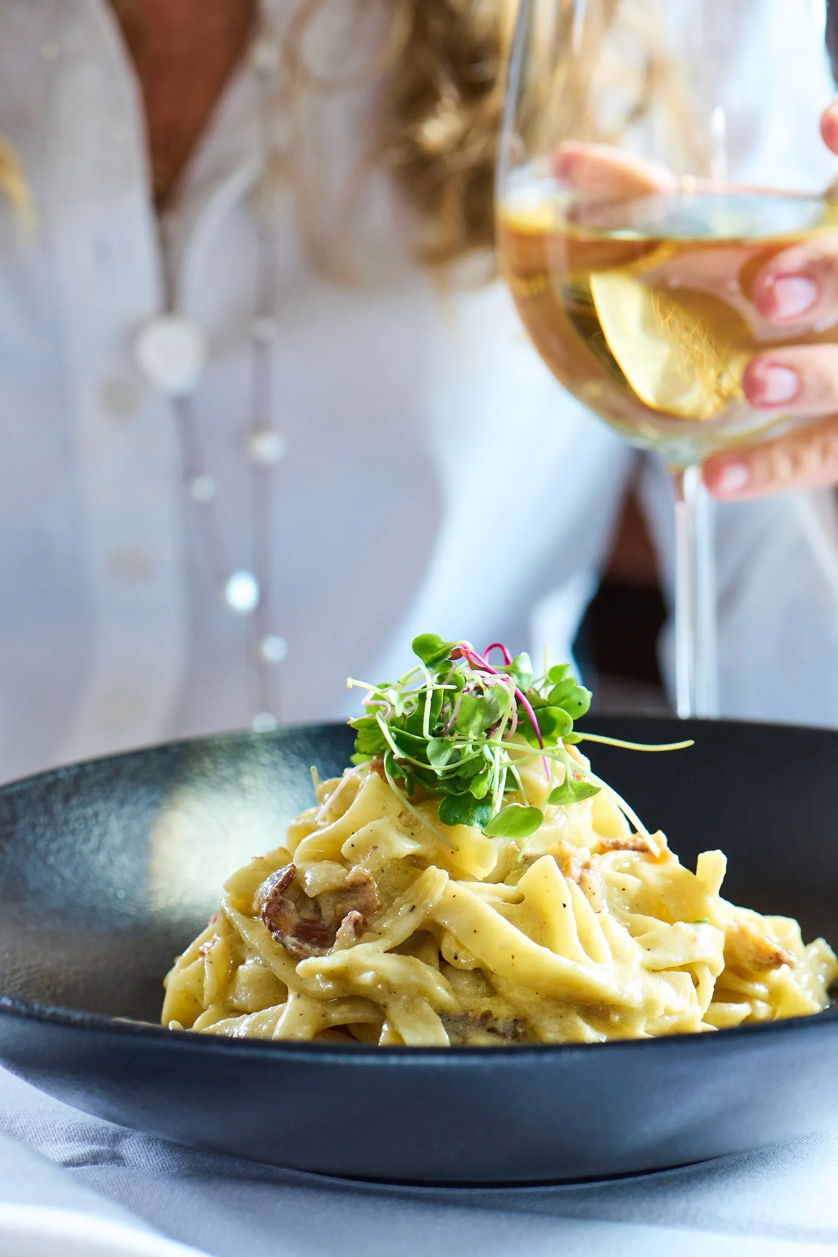 Creamy pasta topped with fresh greens served in a black bowl.