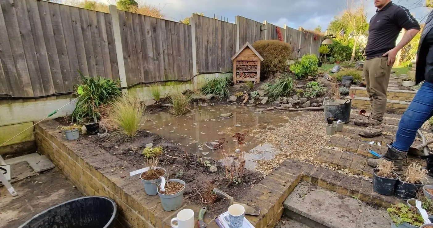 A garden area with scattered debris and plants; a person working nearby, seen from a distance.