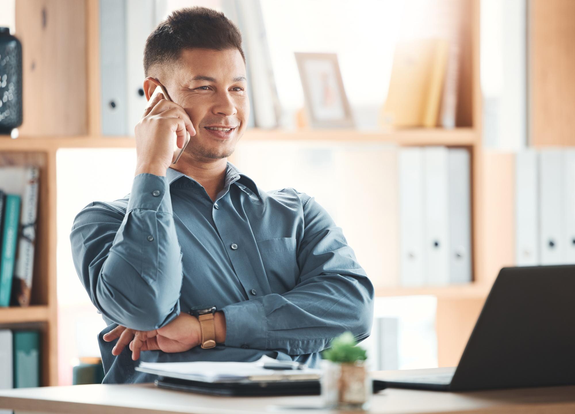 Ondernemer aan zijn bureau met een glimlach aan de telefoon, laptop op de achtergrond