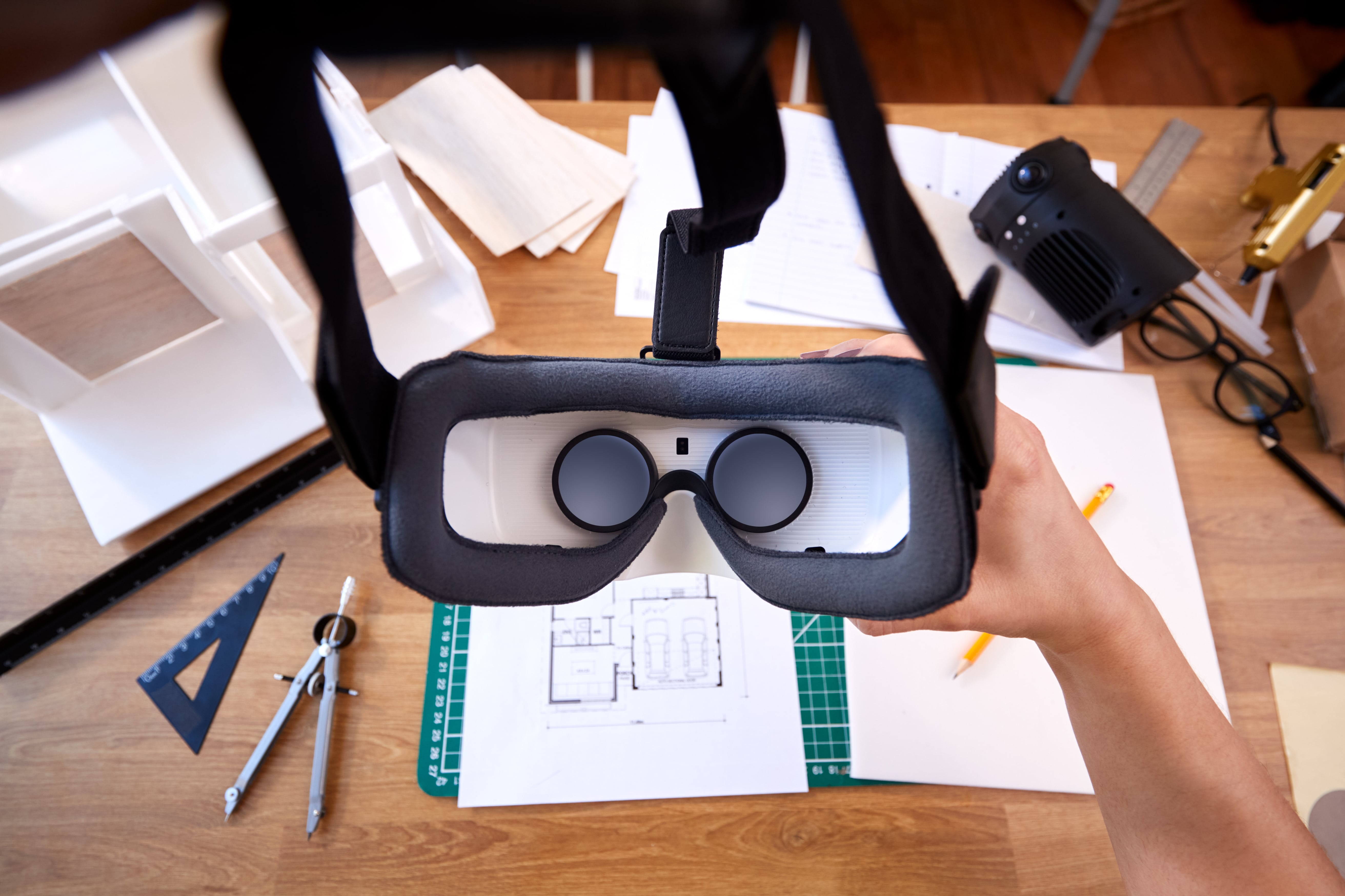 An architect holds a VR headset over a desk with blueprints, showcasing the use of virtual reality for architectural visualization and design.