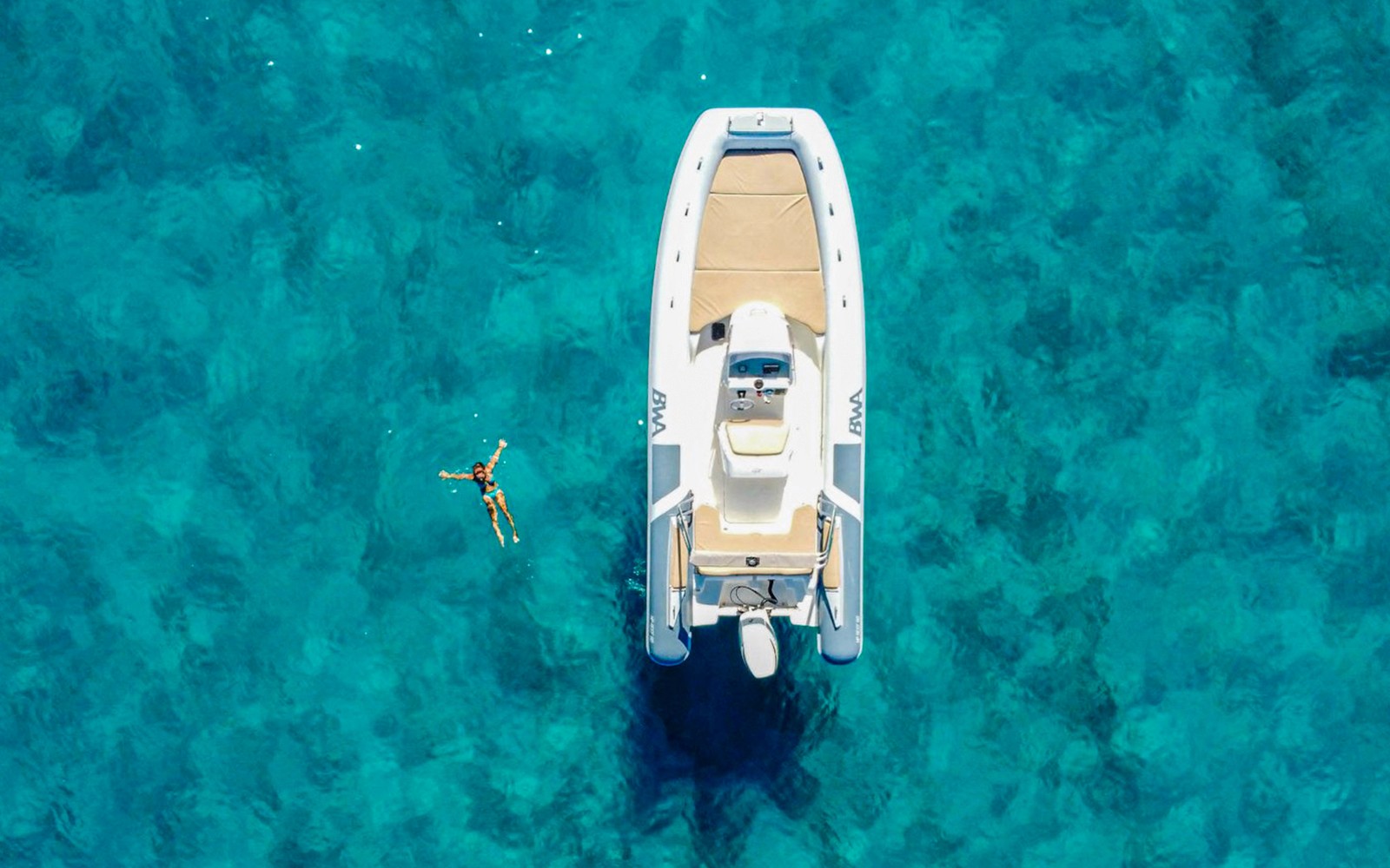 Boat and swimmer in clear blue waters, Gulf of Cagliari tour.