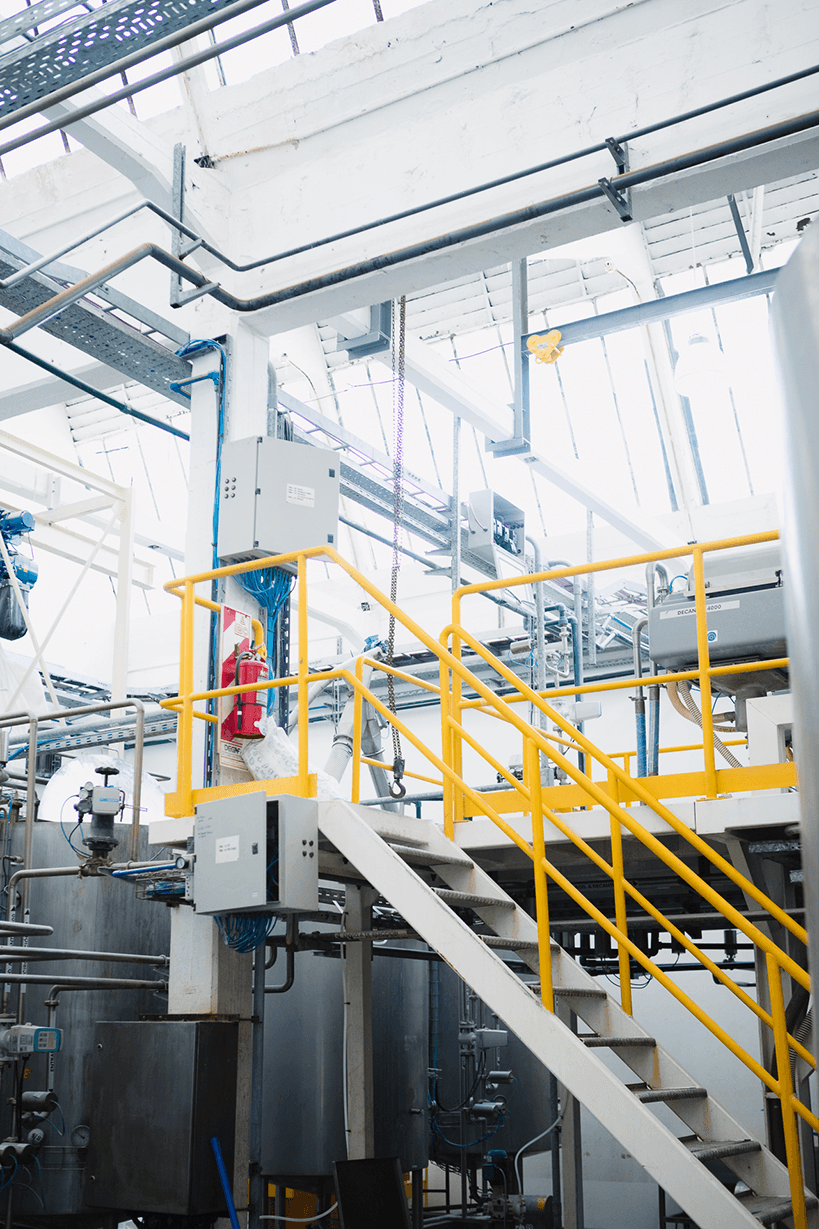 Metal staircase with yellow safety railings inside a modern industrial processing plant.