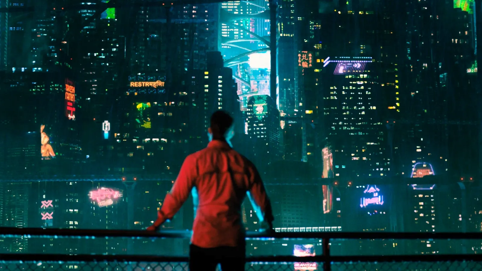 A man stands on a balcony overlooking a vibrant, futuristic cityscape illuminated by colourful neon lights and digital billboards at night.