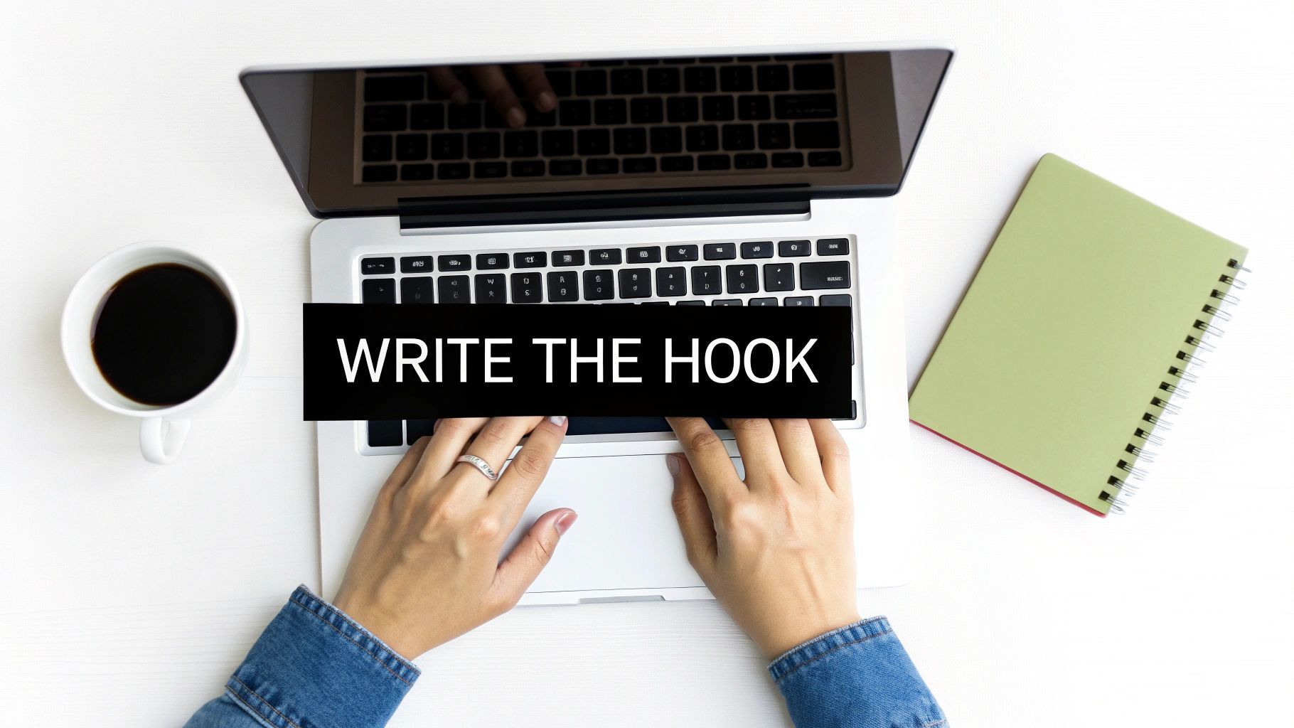 Overhead view of hands typing on a laptop with a coffee and notebook, text says 'WRITE THE HOOK'.