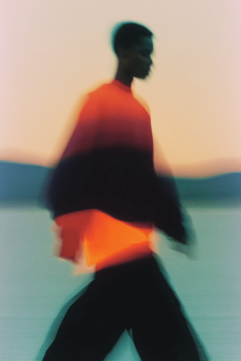 A silhouetted figure walks against a gradient background, wearing an orange and black oversized sweater.