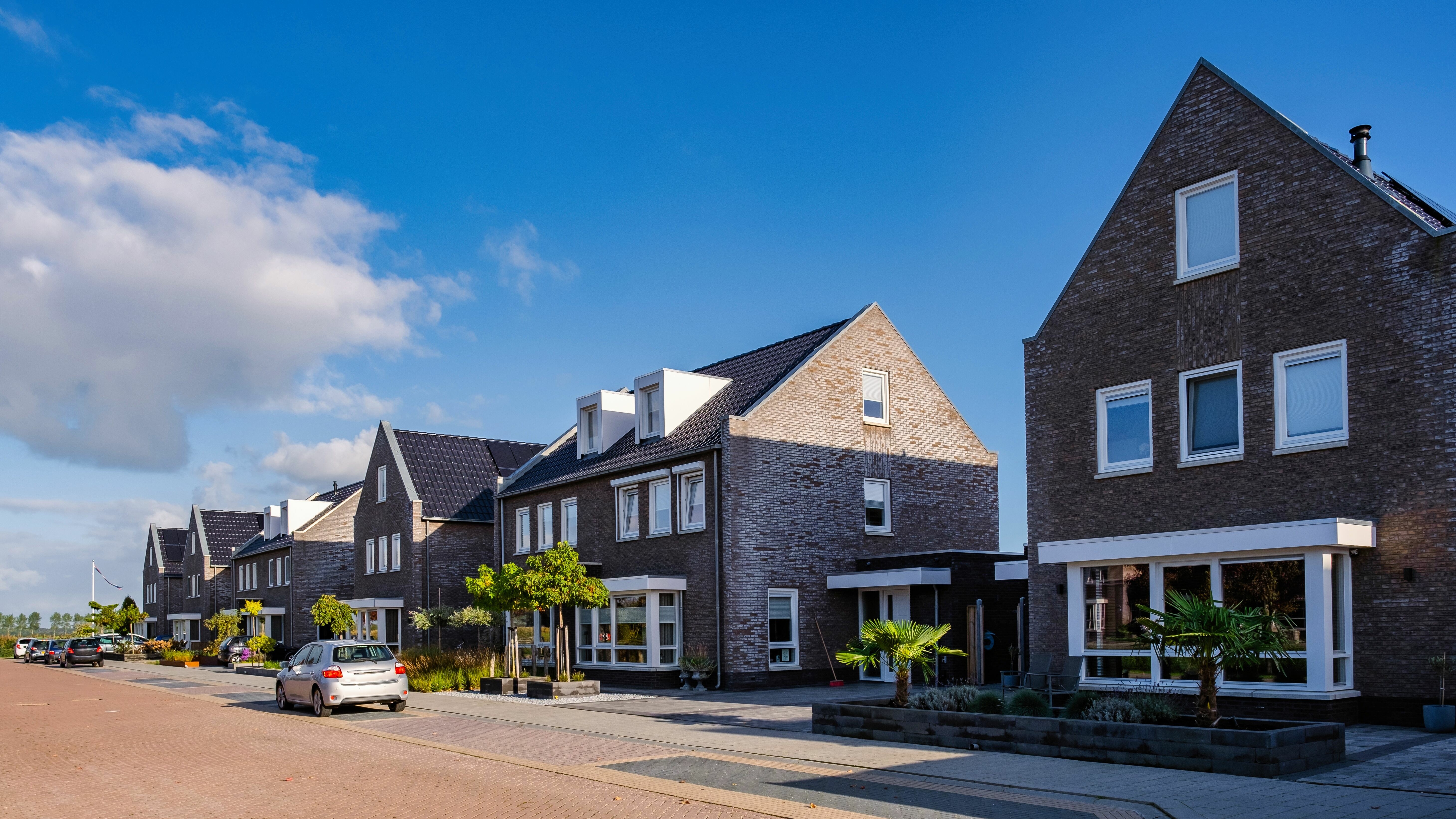 Rij moderne huizen in de buitenwijk met geparkeerde auto's op een zonnige dag.