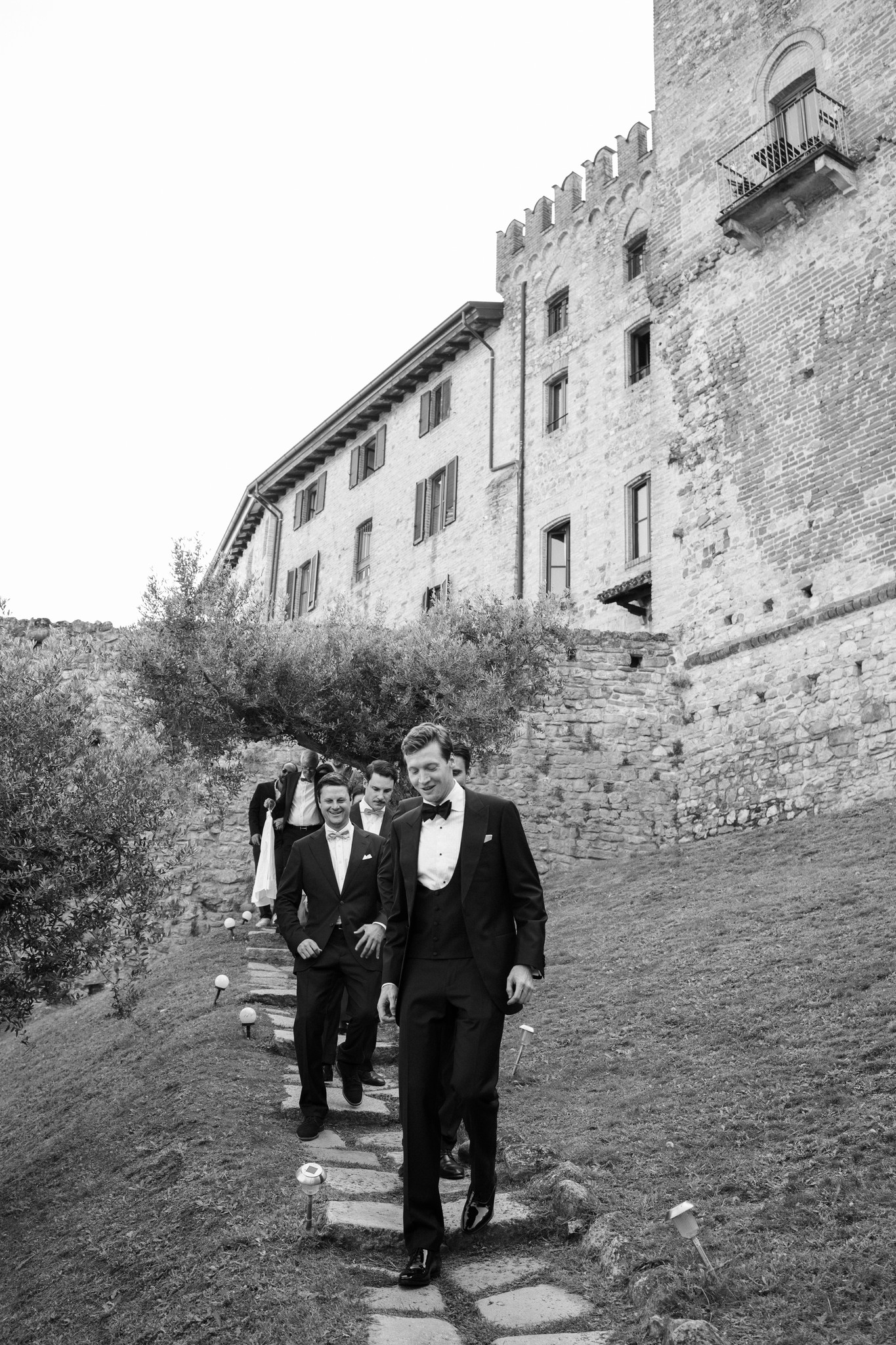 Eline e Antoine camminano verso il Castello di Tabiano, sposi in smoking davanti alle mura medievali, reportage matrimonio