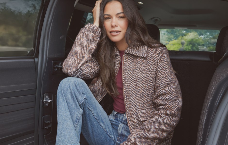 A young woman in classic modern clothes sat in a car in the countryside