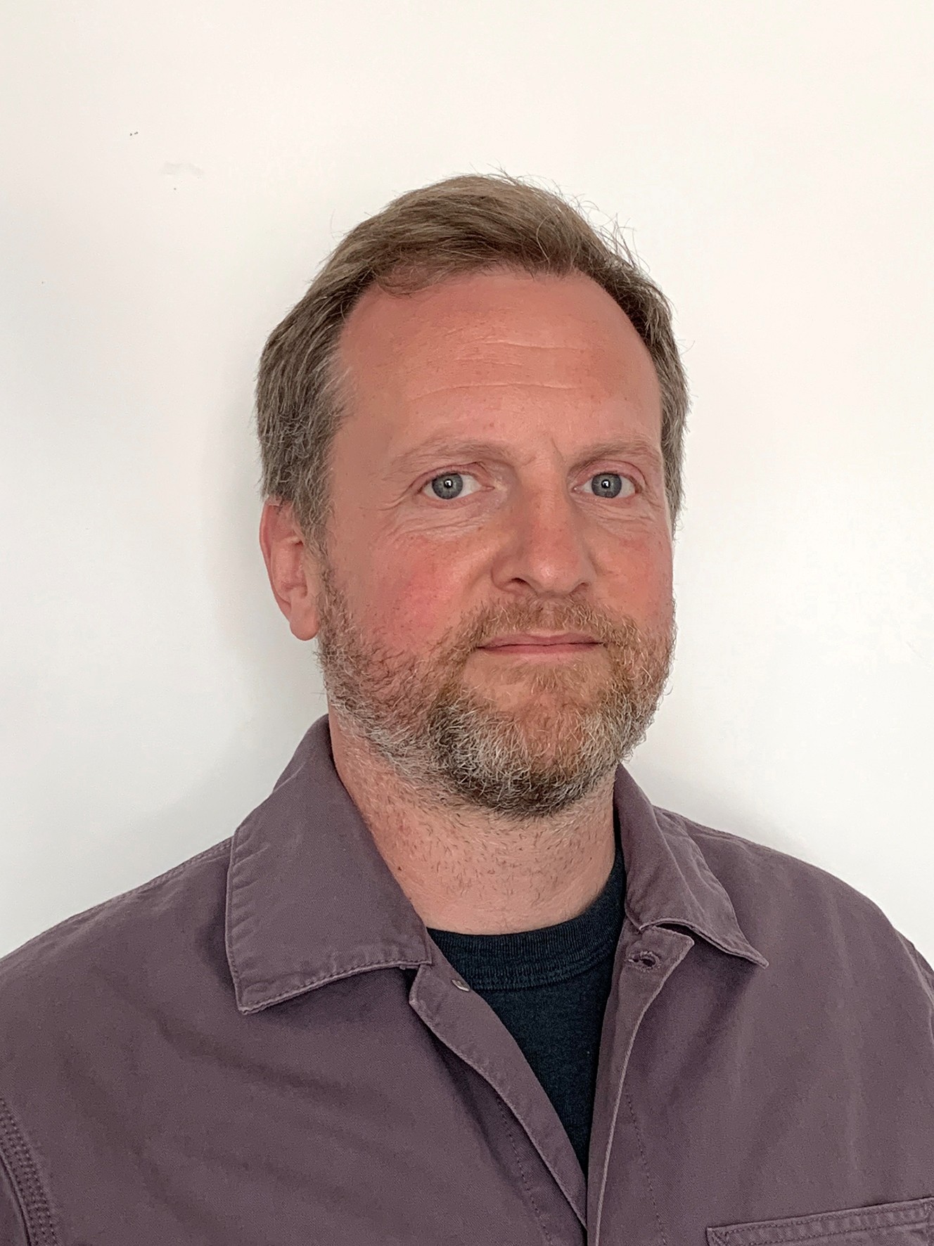 A man infront of a white background wearing a purple blazer.