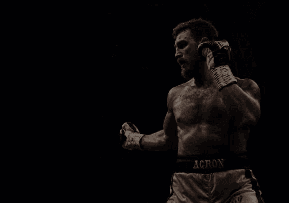 Hero shot of a Agron Smaski boxing coach throwing a focused punch with headline overlay — personal boxing training in Dubai.