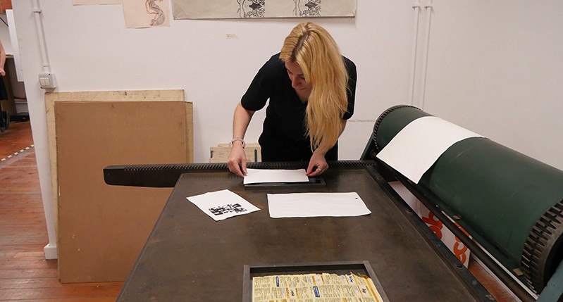 Student adjusting some paper on a pressing bench.
