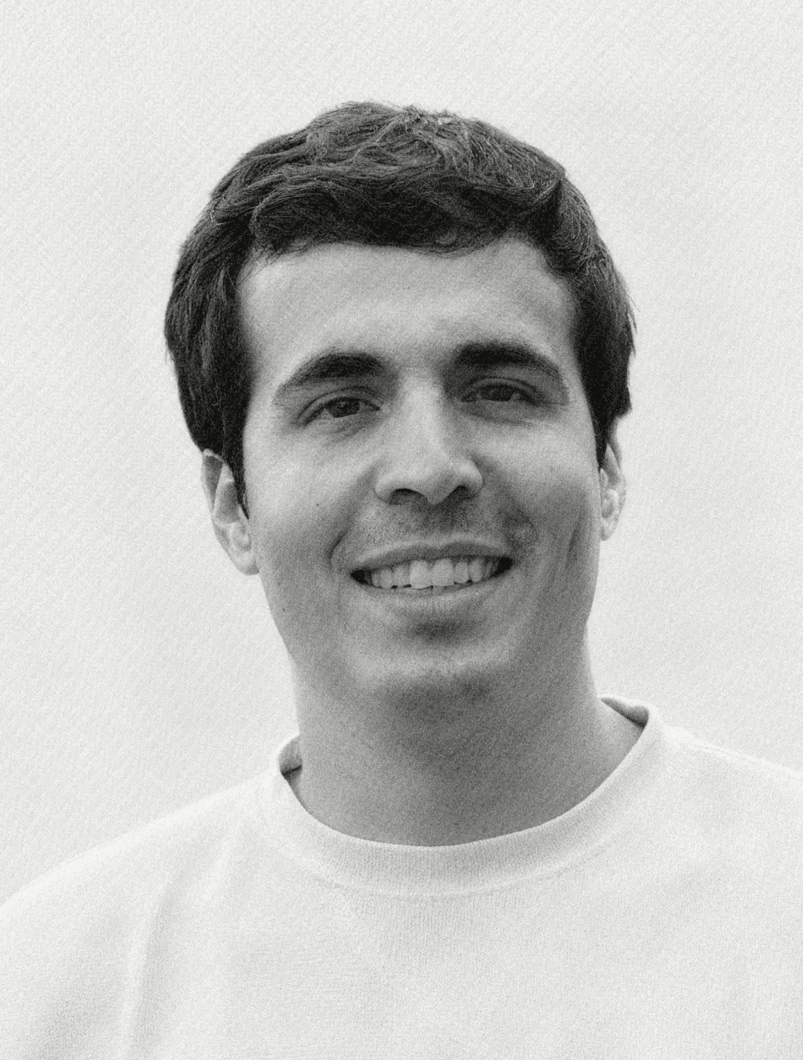 Portrait of a young man with short hair, wearing a dark t-shirt, against a plain background.