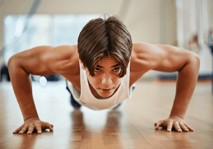 Umięśniony nastolatek wykonuje pompkę na sali gimnastycznej