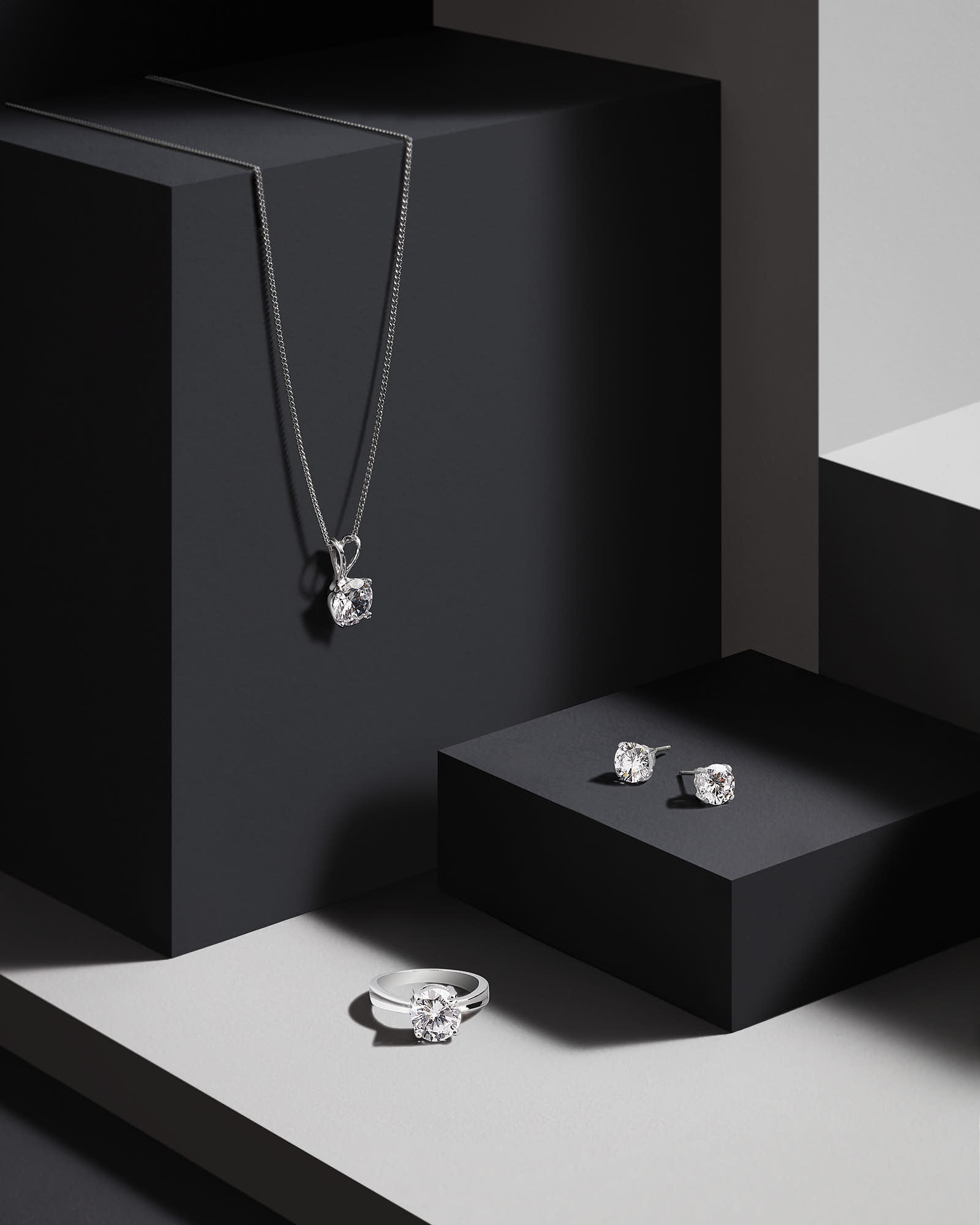 Jewelry displayed on a minimalist black and white surface, featuring a pendant necklace and earrings in elegant boxes.