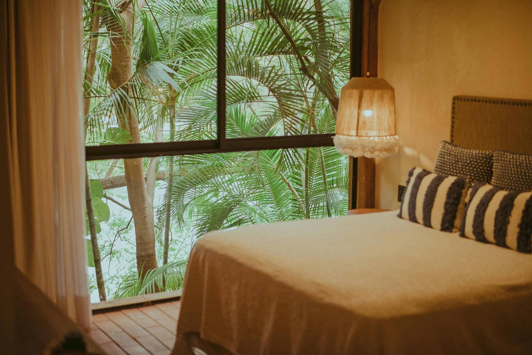 Comfortable resort room with natural light, simple bedding, and tropical greenery outside.
